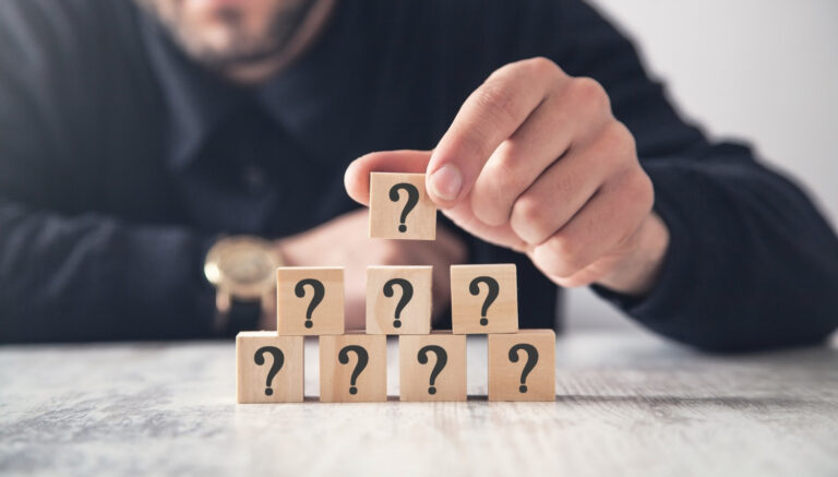 A man stacking wooden blocks with question marks on them, depicting the question, "Are Your CX Questions Out of Order?"